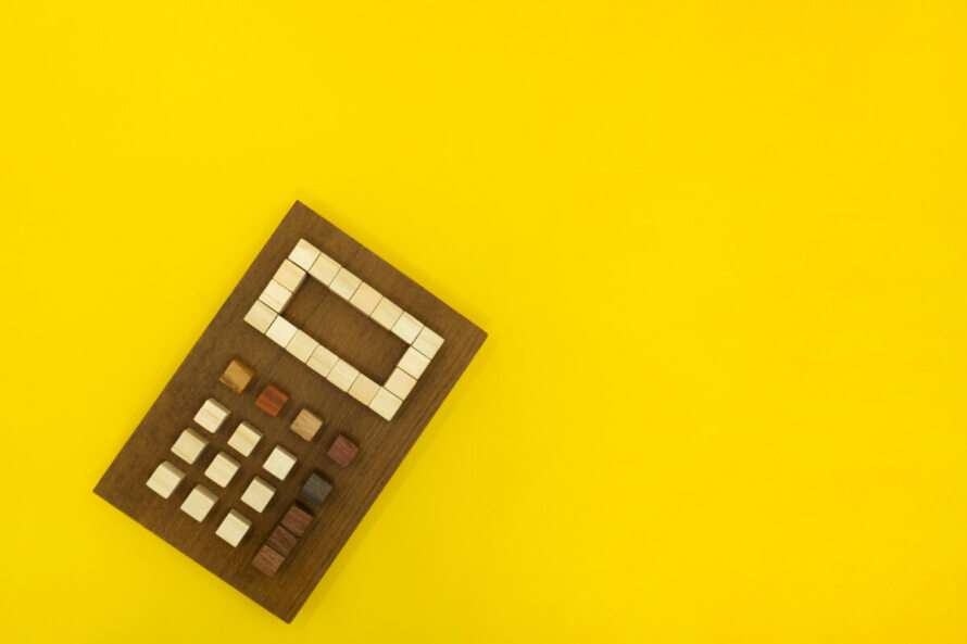 木の素材で形を作った天然の電卓が左下に傾いて置かれている黄色い装飾素材